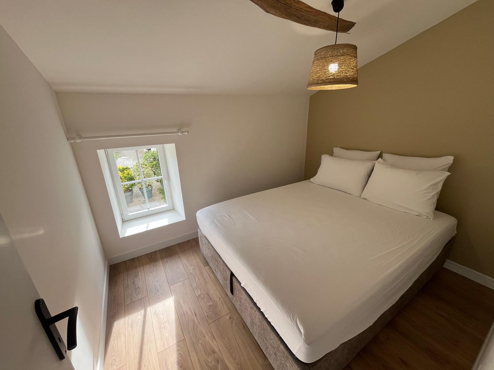 Chambre lumineuse avec lit queen size, poutre apparente et vue sur le jardin