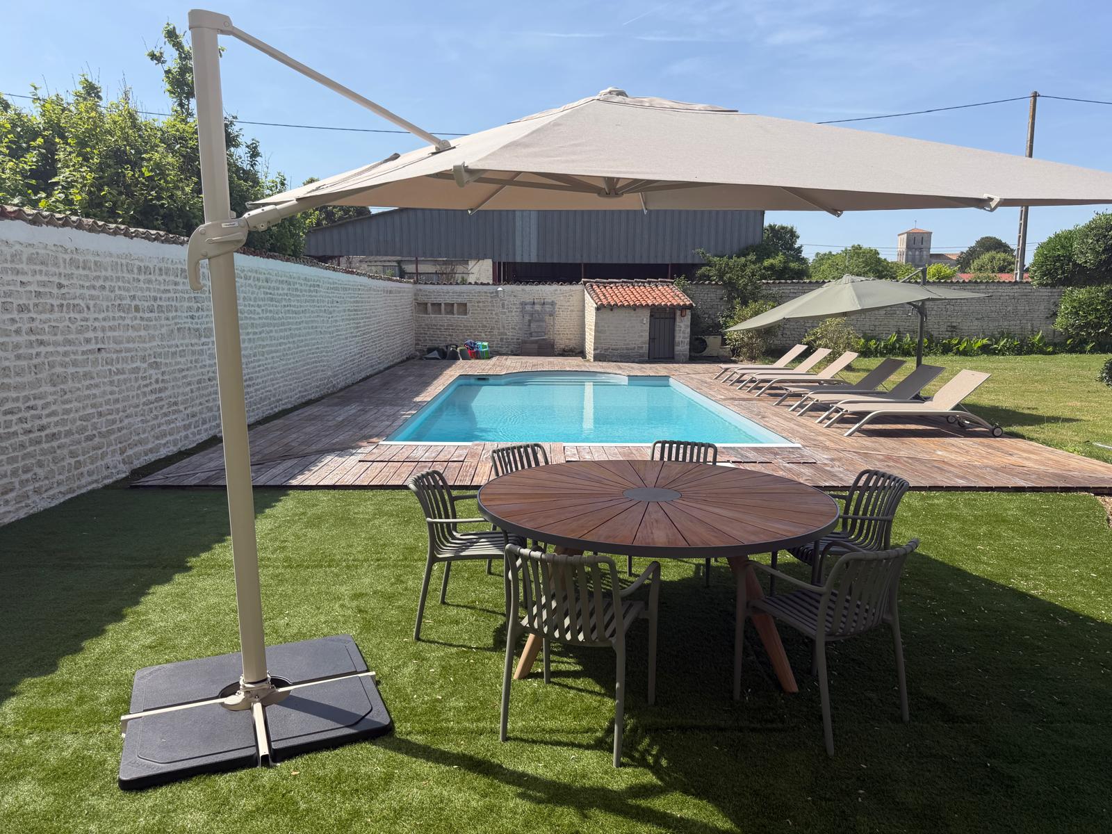 Espace repas extérieur avec table ronde et grand parasol près de la piscine