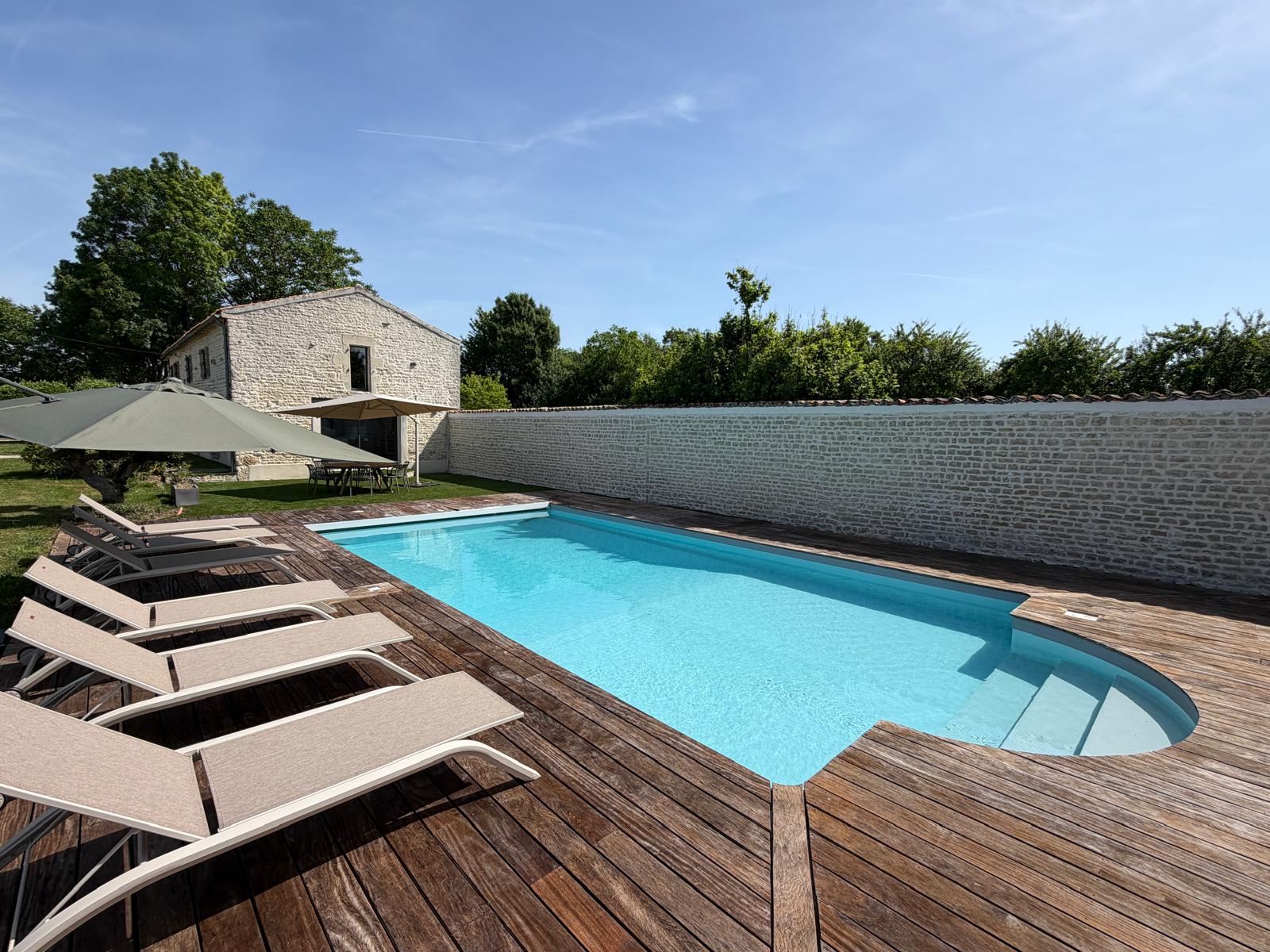 Piscine privée avec terrasse en bois et transats face à l'ancienne dépendance en pierre